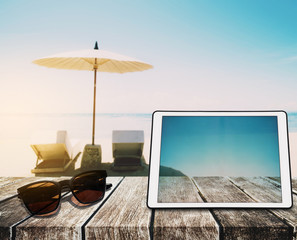 The Beach Holidays, wooden table top, with digital tablet and sunglasses on blurred defocus blue sea and white sand beach in sunrise background