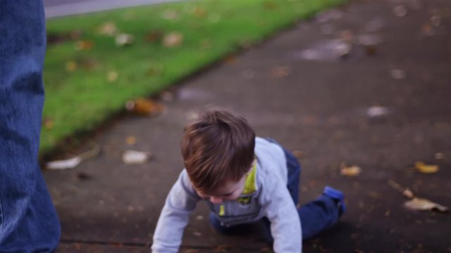 Adorable little boy trips and falls while walking, starts crying, and his dad picks him up