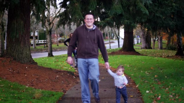 Adorable little boy holding his dad's hand while walking in a park on a fall day