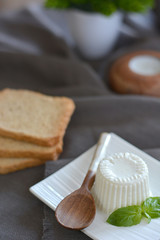fresh cheese with basil leaves on a white plate and a table with