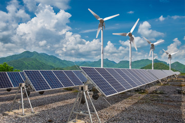 Renewable energy concept. Solar panels with wind turbines against mountanis landscape against blue...
