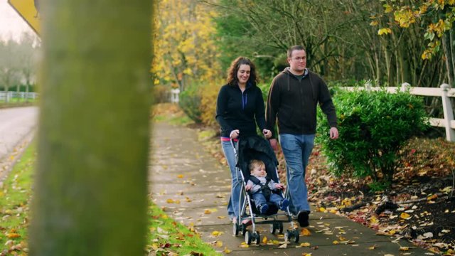 Parents on a walk pushing their little boy in a stroller, on a fall day