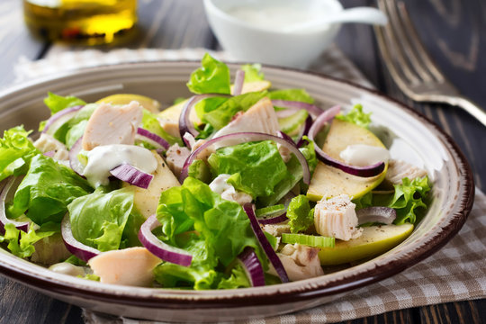 Salad with lettuce, apple, celery, onion and chicken on the gray plate on dark wooden background.Selective focus