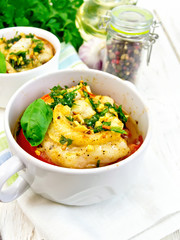Fish baked with tomato and garlic in white bowl on board