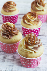 Vanilla cupcakes with a cap of cream on white wooden table