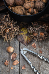 Haselnüsse und Walnüsse in einer Eisenpfanne mit Herbstlaub und einem Nussknacker auf einem alten Holzuntergrund