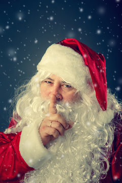 Santa Claus presses a finger to his lips.