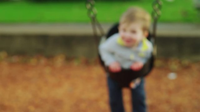 Adorable little boy on a swing in slow motion, with a big smile on his face