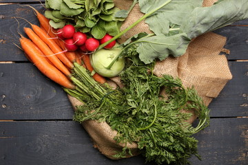 radish, kohlrabi and carrots on wooden background and jute bag