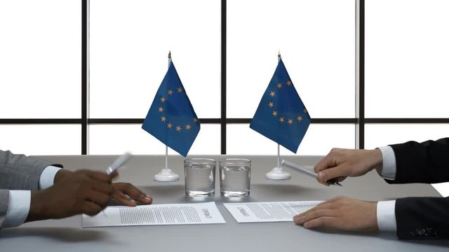 Hands of men signing papers. Handshake near EU flags. Acquire new allies. Mutual respect and common goals.