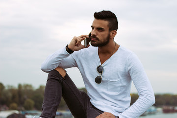 Handsome man talking on the phone outdoors. With leather jacket, sunglasses, a guy with beard. Instagram effect.
