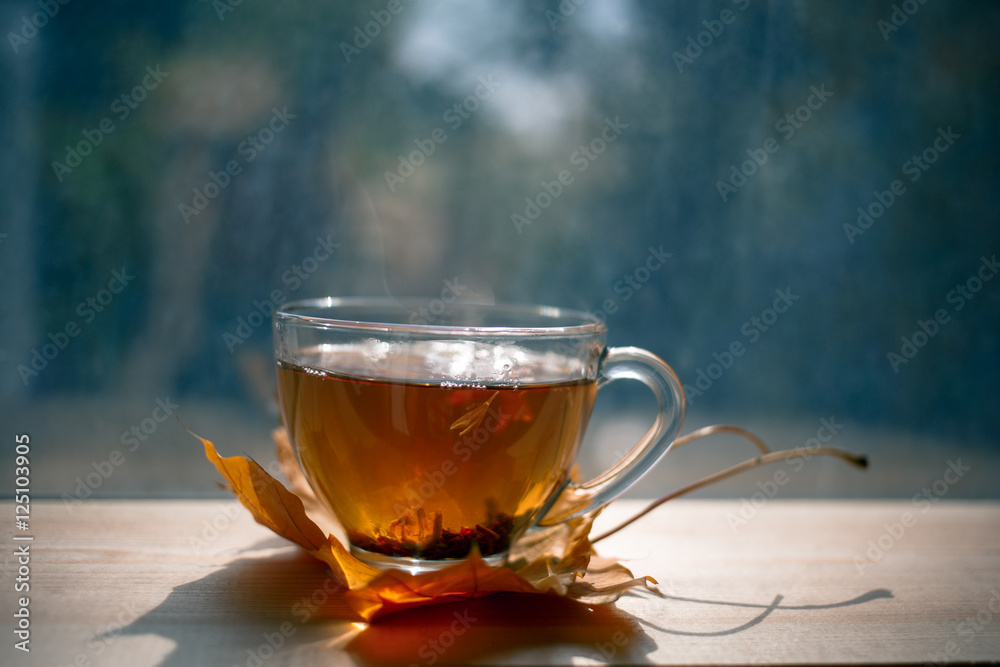 Wall mural autumn still life: tea on maple leaves on a wooden table near the window. the sun's rays on a cup of