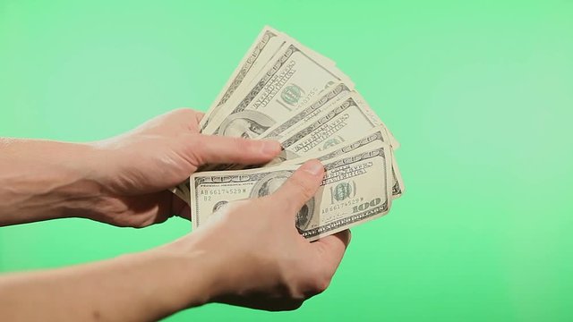 Close up of hands counting various united states dollar notes over green background.