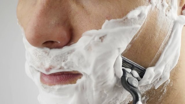 Man shaving with foam and manual razer. Close up of man shaving beard.
