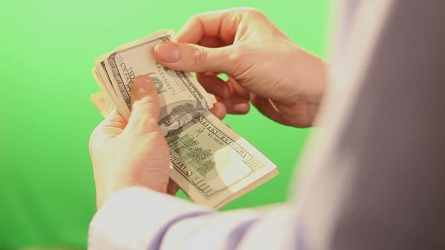 Slowly counting US dollar banknotes. Filmed behind a green isolated background and in close up. 
