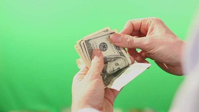 Pair of hands slowly counting American Dollar bills in hundreds. Filmed behind a green isolated screen. 