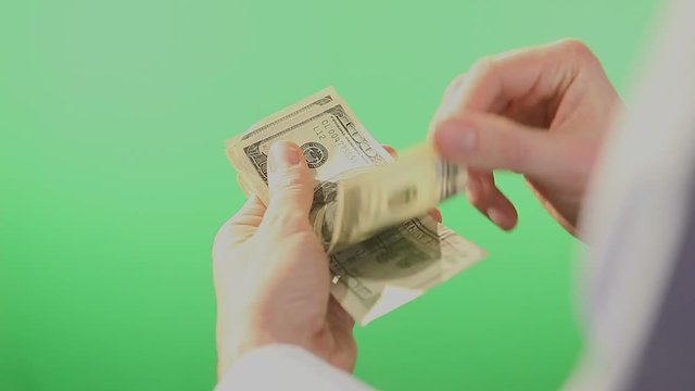 Pair of hands slowly counting folded American Dollar bills in hundreds. Filmed behind a green isolated screen.