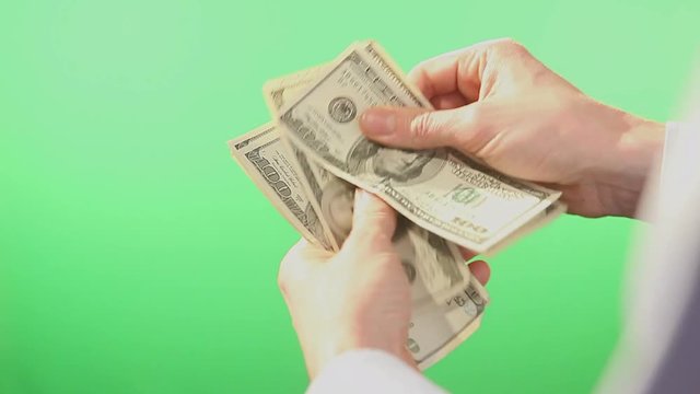 Pair of hands slowly counting American Dollar bills in hundreds. Filmed behind a green isolated screen.
