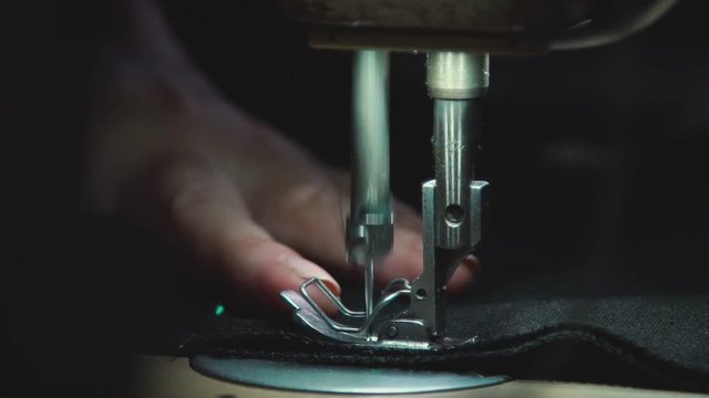 Sewing needle with thread at working sewing machine. Needle with thread stitching seam on fabric. Working sewing machine. Manufacturing equipment at factory.