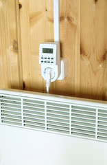 Working white electric convector heater plugged to timer power socket operated in smart house system against wooden wall inside room side view closeup