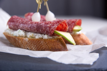 Bruschetta crostini with salami, avocado and ricotta cheese on a slate plate, parchment. Italian cuisine