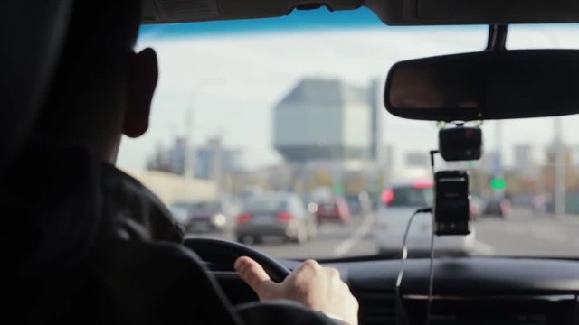 Backview of a man driving a car in a city. Blurred sights. Big interesting building in the distance. Traveling by car.