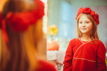 Girl in red wreathe and dress looks in the mirror