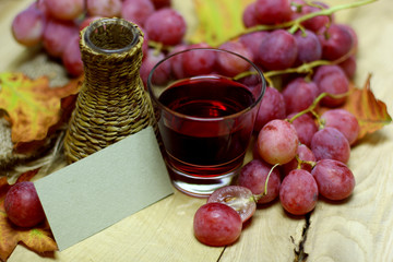 Red rose grapes bunch, wicker bottle, glass with red natural organic house wine, and autumn leaves on wood background design image with blank papers card label place for you text or logo