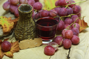 Red rose grapes bunch, wicker bottle, glass with red grape juce or wine, and autumn leaves on wooded background design image with blank vintage handmade paper card label place for you text