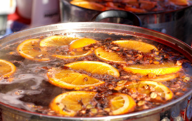 Mulled wine, punch, sangria, with cinnamon, orange, spices and citrus fruit. Hot warming drink cooked in a pan outdoors. Close up.