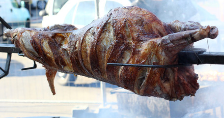 Carcass of a whole pork meat roasting on a spit over hot coals at an outdoor big barbecue - obrazy, fototapety, plakaty