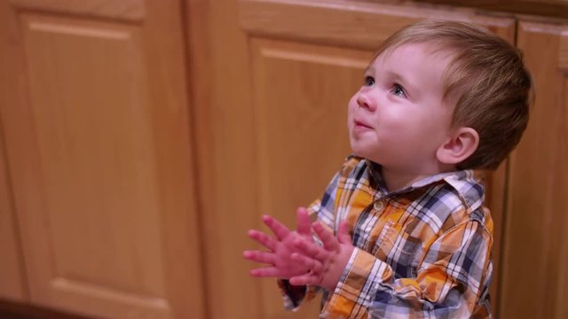 Little boy smiling and clapping in a kitchen, and being fed a spoonful of food