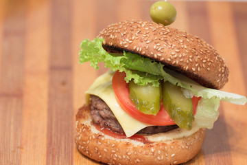 homemade burger with beef cutlet, cucumber, lettuce, onion and yellow cheese on wooden cutting board. closeup shot with negative space