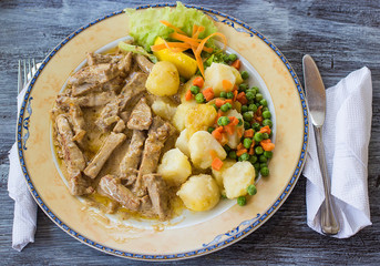 plate with potatos, beans, meat and greens potherbs and cutlery, tableware. on wooden table. from the top point of view. closeup shot. nobody in the frame