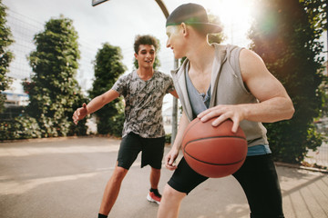 Naklejka premium Two young friends playing basketball on court outdoors