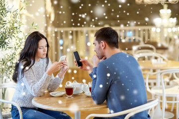 couple with smartphones drinking tea at cafe