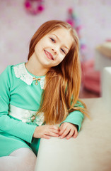 Blonde child in mint dress sits at the white table
