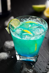 Blue Cocktail with Lemon and Ice on Dark Background