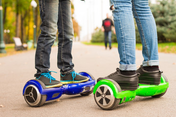 Fototapeta premium Feet of girl and boy riding electric mini segway outdoors in park