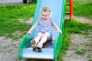 Fototapeta na wymiar Happy little girl on slide in summer park