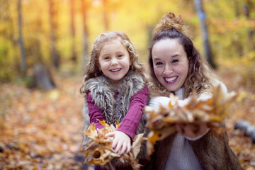Young mother playing with her daughter in autumn park