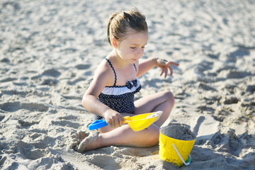 Adorable little girl playing with sand at the beach in summer
