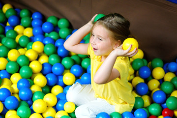 Fototapeta na wymiar Happy little girl playing at colorful plastic balls playground