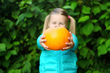 Beautiful smiling girl outdoors holding little pumpkin