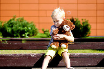 Adorable sad boy with teddy bear in park.