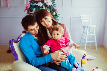 Happy parents sit with their daughter on large beige chair