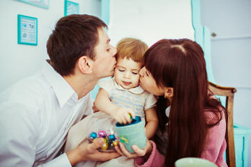 Dad and mom kiss their daughter's cheeks while she plays with cu