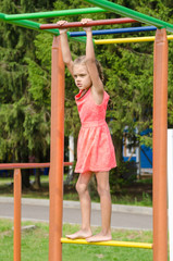 The girl in the pink dress on the horizontal bar climbing on playground