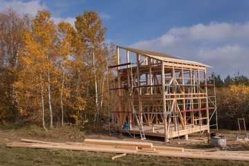 Metal scaffolding around the unfinished house.  Construction of ecological house. Wooden frame of house under construction.Framed New Construction of a House. Timber house in building process
