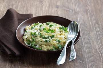 Tagliatelle pasta with green peas, leek and cream sauce on the wooden table 